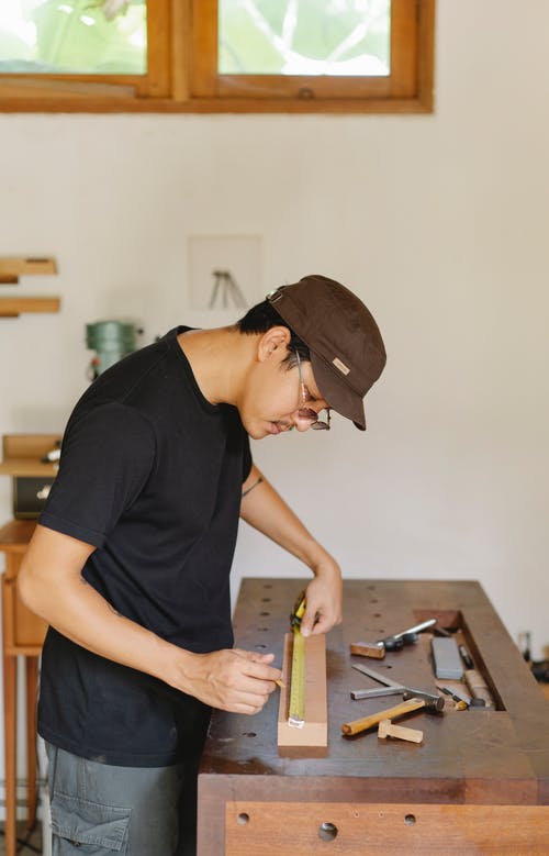 族裔木匠测量木板在车间 · 免费素材图片
