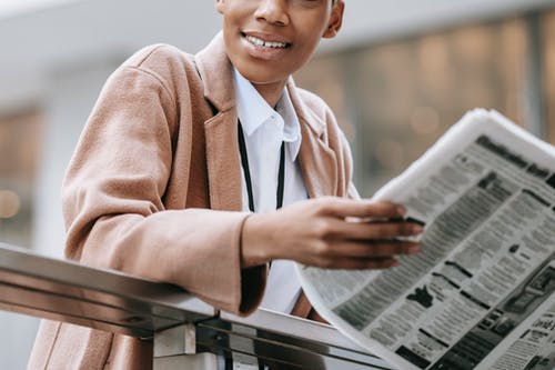 微笑着棕色的外套，拿着报纸的女人 · 免费素材图片