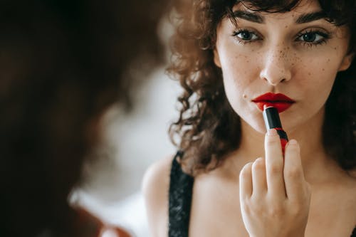 拿着红色唇膏的白色背心的女人 · 免费素材图片