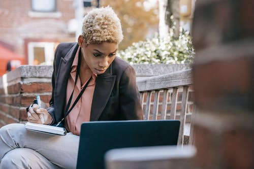 黑色西装外套坐在椅子上使用macbook的女人 · 免费素材图片