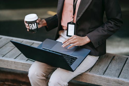 黑色西装外套和棕色的裤子，坐在黑色的笔记本上的棕色木凳上的人 · 免费素材图片