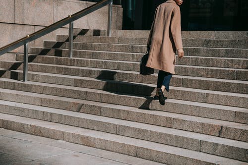 棕色外套和黑色的裤子，在灰色的混凝土楼梯上行走的女人 · 免费素材图片