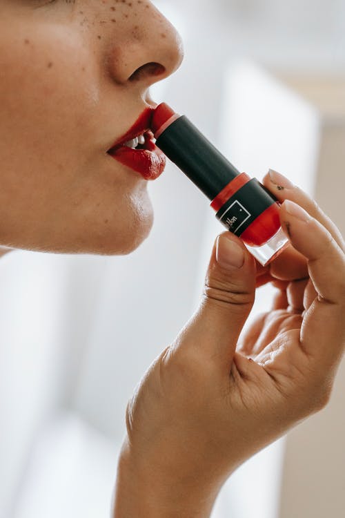 女人把红色的唇膏放在她的嘴唇上 · 免费素材图片