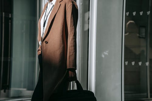 站在白色的墙壁旁边的棕色外套的女人 · 免费素材图片