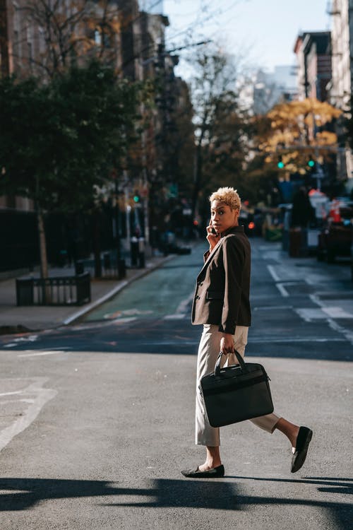 穿黑夹克的男人背着棕色皮包走在大街上 · 免费素材图片