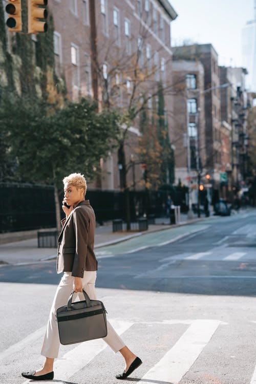 黑色外套和棕色皮革吊袋站在人行道上的女人 · 免费素材图片