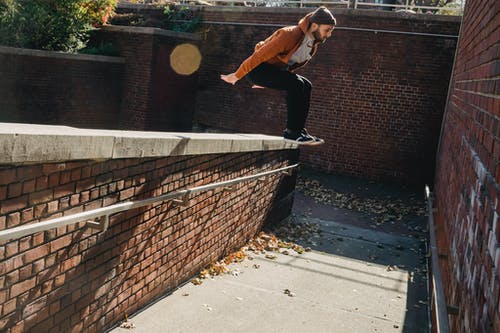 黑色外套和棕色的裤子，在灰色的混凝土路上跳跃的人 · 免费素材图片