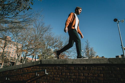 红色和白色的外套和黑色的裤子，坐在混凝土墙上的男人 · 免费素材图片