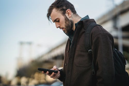 拿着智能手机的黑大衣的男人 · 免费素材图片