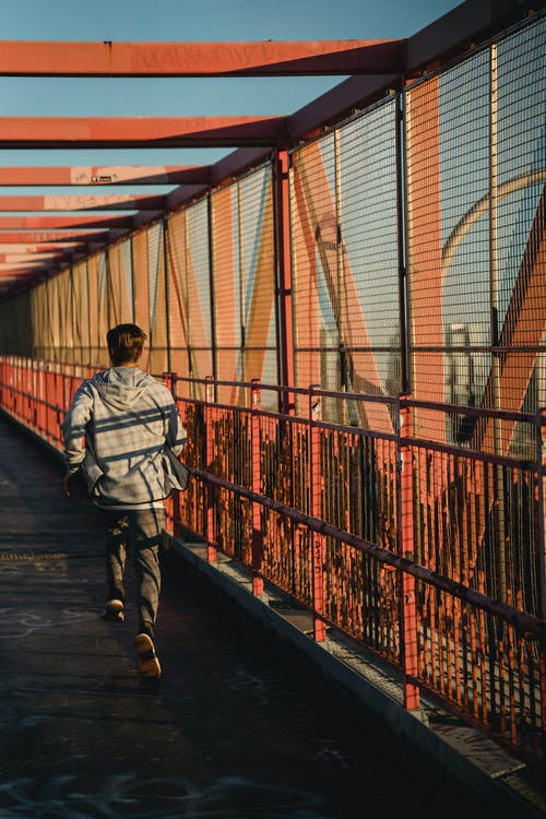 灰色外套和黑色的裤子，在红桥上行走的人 · 免费素材图片