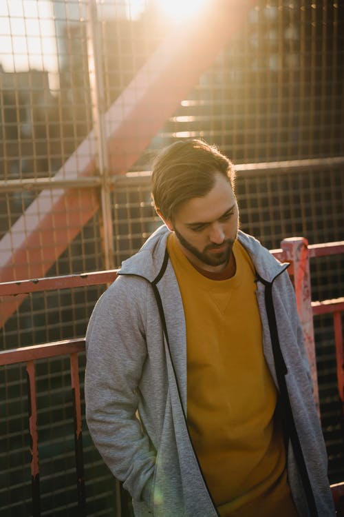 站在红色金属栅栏旁边的黄色衬衫和灰色羊毛衫的女人 · 免费素材图片