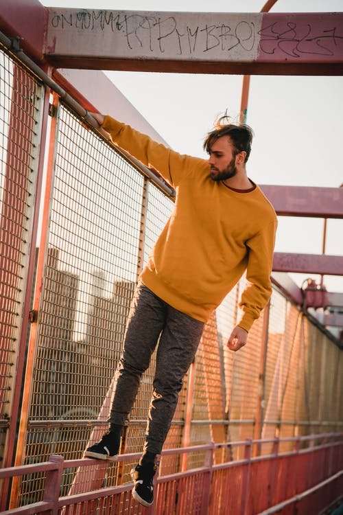 黄色毛衣和蓝色牛仔牛仔裤，站在棕色木桥上的男人 · 免费素材图片