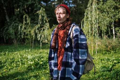 蓝色和白色格子礼服衬衫和红色针织帽站在绿草上的女人 · 免费素材图片