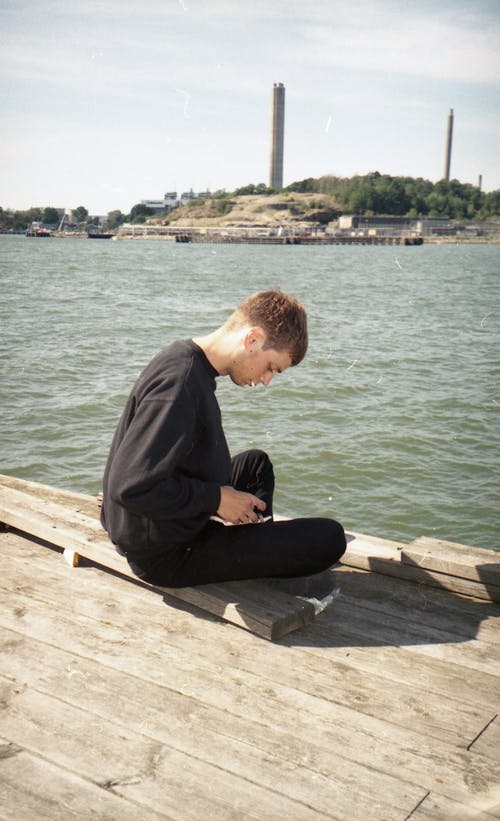 坐在棕色的木码头上的黑色长袖衬衫的男人 · 免费素材图片