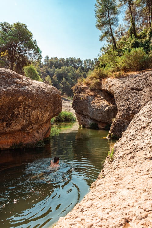 匿名游客在森林里的岩石峭壁之间的湖里游泳 · 免费素材图片