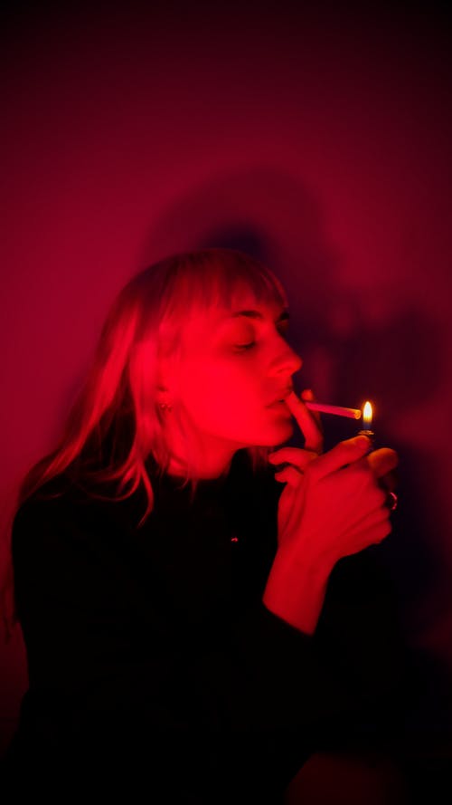 拿着点燃的香烟棒的粉红色头发的女人 · 免费素材图片