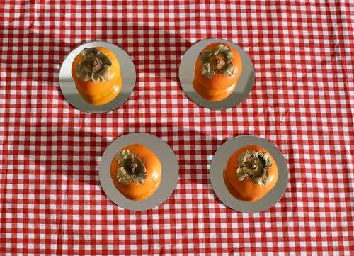 成熟的明亮橙色柿子放在方格桌布的盘子上 · 免费素材图片