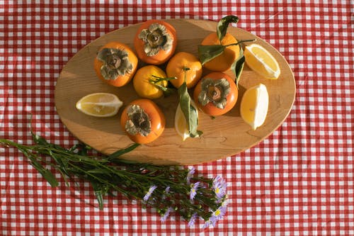 柿子与洋甘菊花附近的木板上的橘子 · 免费素材图片