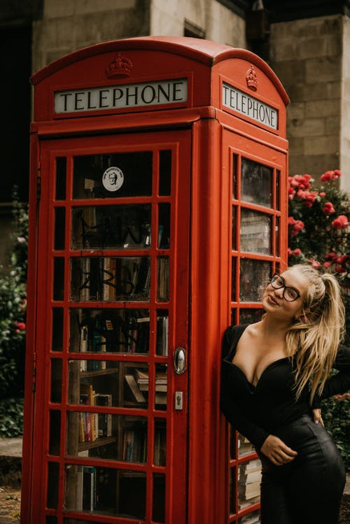 黑色背心站在红色电话亭旁边的女人 · 免费素材图片