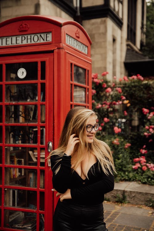 黑色长袖衬衫站在红色电话亭旁边的女人 · 免费素材图片