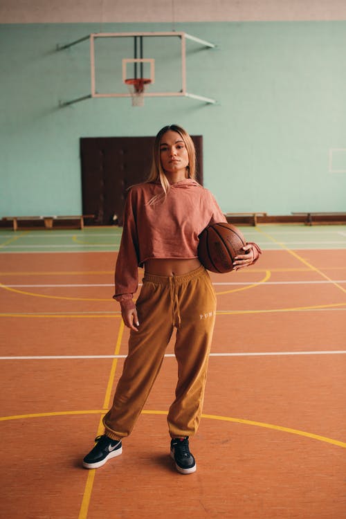 棕色皮夹克和棕色的裤子，站在篮球场上的女人 · 免费素材图片