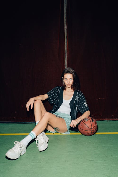 黑色和白色的圆点衬衫和蓝色牛仔短裤，坐在篮球上的女人 · 免费素材图片