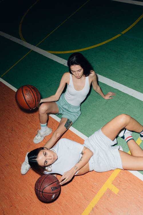 女子拿着球躺在篮球场上 · 免费素材图片