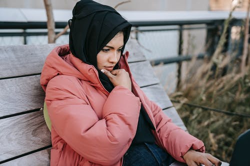 粉红色的外套和蓝色牛仔牛仔裤，坐在棕色木地板上的女人 · 免费素材图片