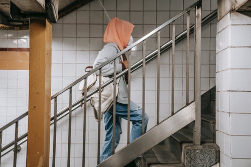 蓝色牛仔牛仔裤和橙色连帽衫站在灰色的混凝土楼梯上的男人 · 免费素材图片