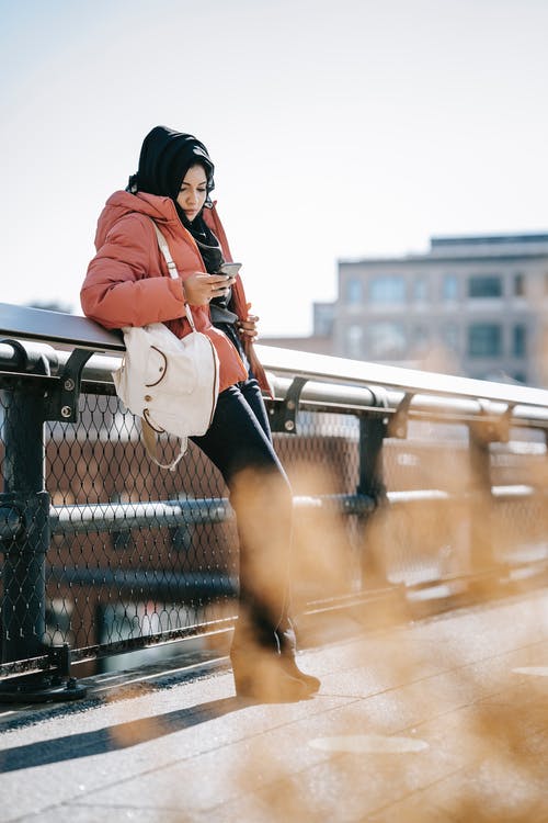 橙色外套和黑色的裙子，坐在黑金属栅栏上的女人 · 免费素材图片