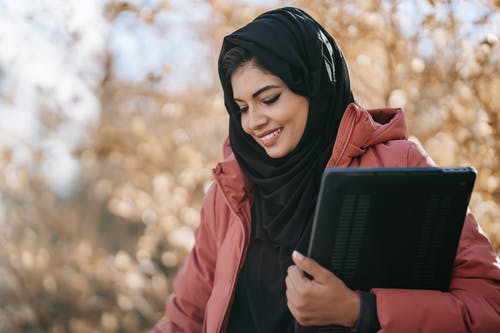 黑色的头巾和棕色的外套，拿着黑色的手提电脑的女人 · 免费素材图片