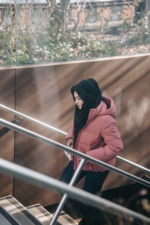 站在棕色木墙旁边的红色连帽衫的女人 · 免费素材图片