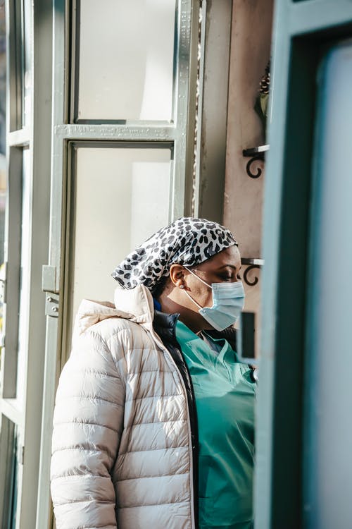 白色和黑色的针织帽和绿色外套站在蓝色木门旁边的女人 · 免费素材图片