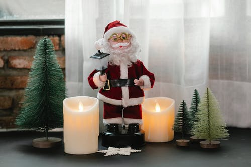 蜡烛旁边的圣诞老人公仔 · 免费素材图片