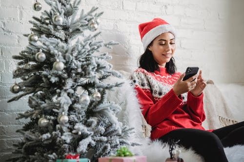红色和白色的圣诞老人的帽子，拿着黑色的智能手机的女人 · 免费素材图片