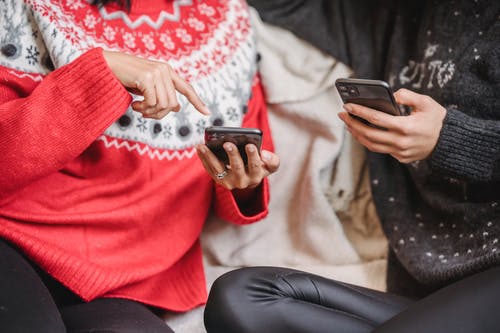 红色毛衣和黑色的裤子，拿着黑色的智能手机的女人 · 免费素材图片