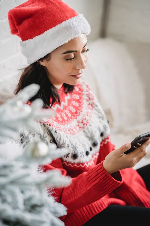 拿着黑色智能手机的红色和白色针织毛衣的女人 · 免费素材图片
