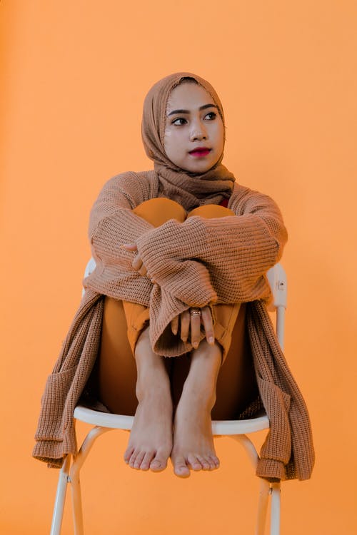 坐在白色的塑料椅子上的棕色针织毛衣的女人 · 免费素材图片
