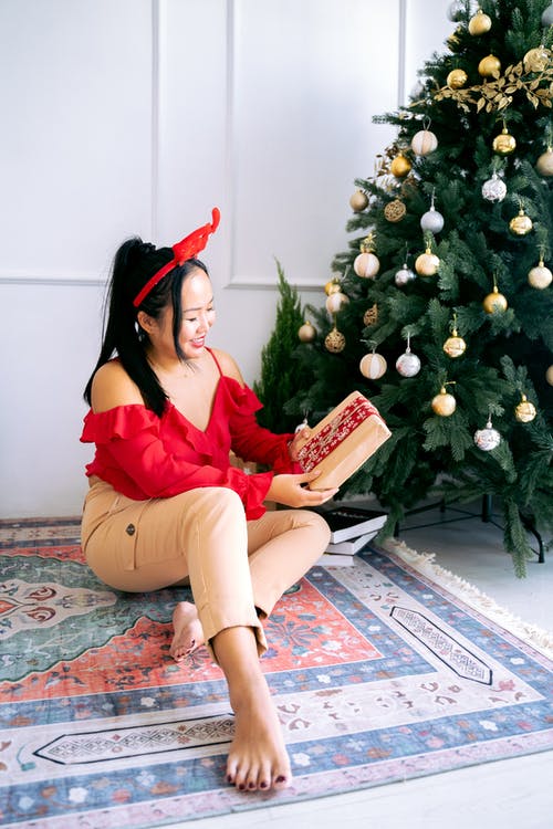 坐在圣诞树旁边的地板上的红裙子的女人 · 免费素材图片