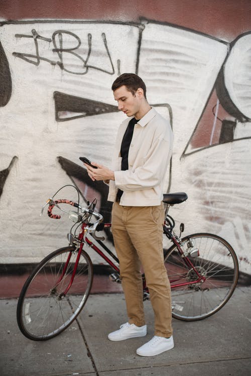 白色礼服衬衫和黑色背心站在红色自行车旁边的人 · 免费素材图片