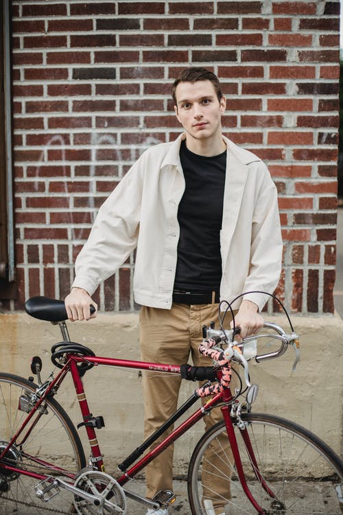 站在红色自行车旁边的白夹克和棕色裤子的人 · 免费素材图片