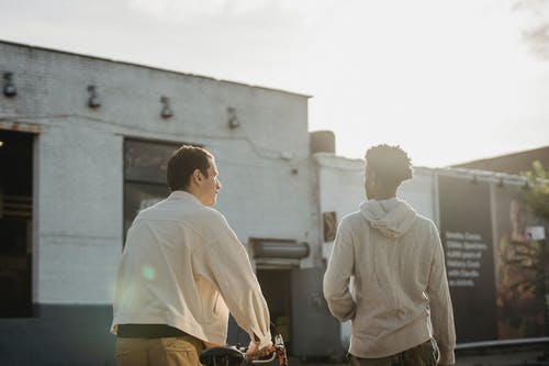 白色长袖衬衫和棕色裤子站在绿色衬衫的男人旁边的男人在 · 免费素材图片