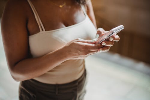 白色运动文胸和黑色牛仔短裤，拿着智能手机的女人 · 免费素材图片