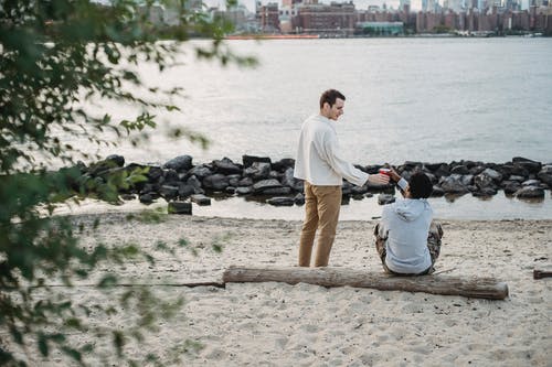 穿着白衬衫和棕色短裤的男人站在水附近的棕色沙滩上 · 免费素材图片
