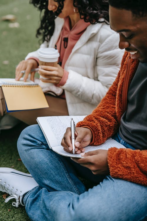 拿着白色钢笔的棕色针织衫和蓝色牛仔牛仔裤的女人 · 免费素材图片