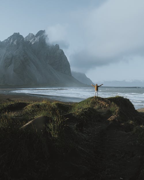 站在水体附近的棕色岩石上的人 · 免费素材图片