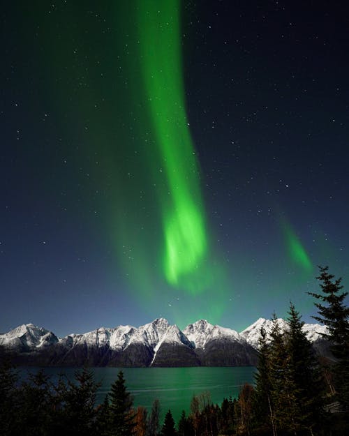 夜晚的星星在绿色天空下的雪覆盖的山 · 免费素材图片