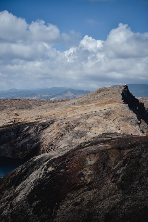 在白云和蓝天下的蓝色大海旁边的棕色和绿色山 · 免费素材图片