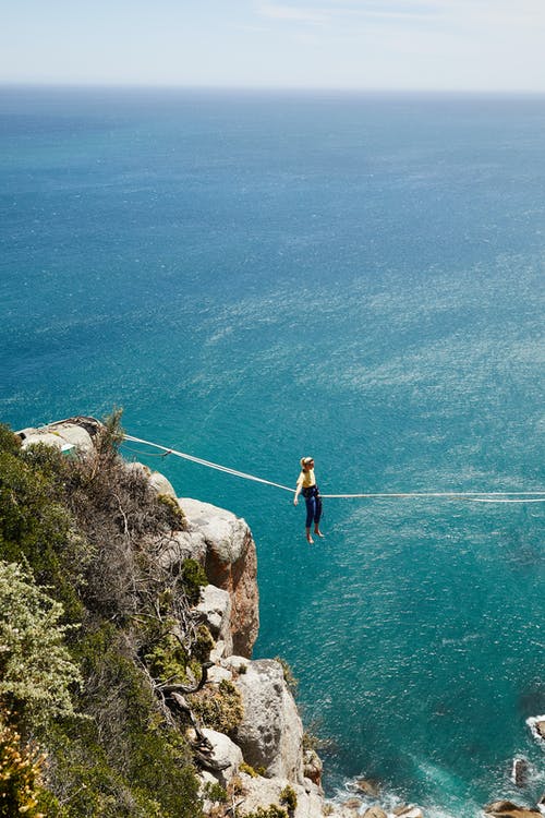 黑色衬衫和蓝色牛仔牛仔裤的男人站在水体附近的岩层上 · 免费素材图片