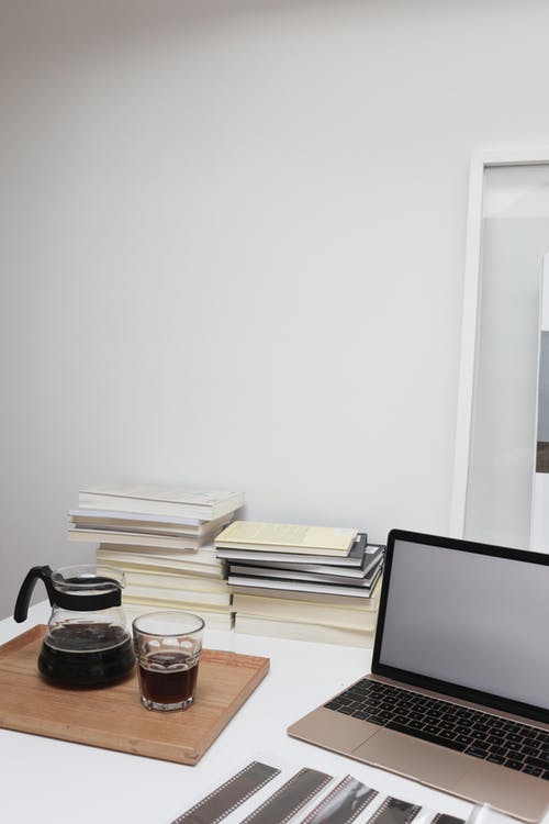 笔记本电脑放在靠近咖啡杯和一叠书的桌子上 · 免费素材图片